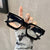 Black glasses held by a hand with decorative nails against a neutral background