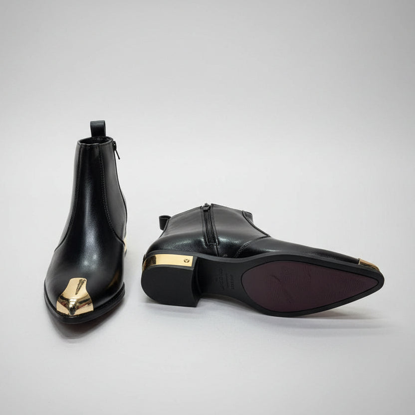 Black ankle boots with gold toes on a wooden floor